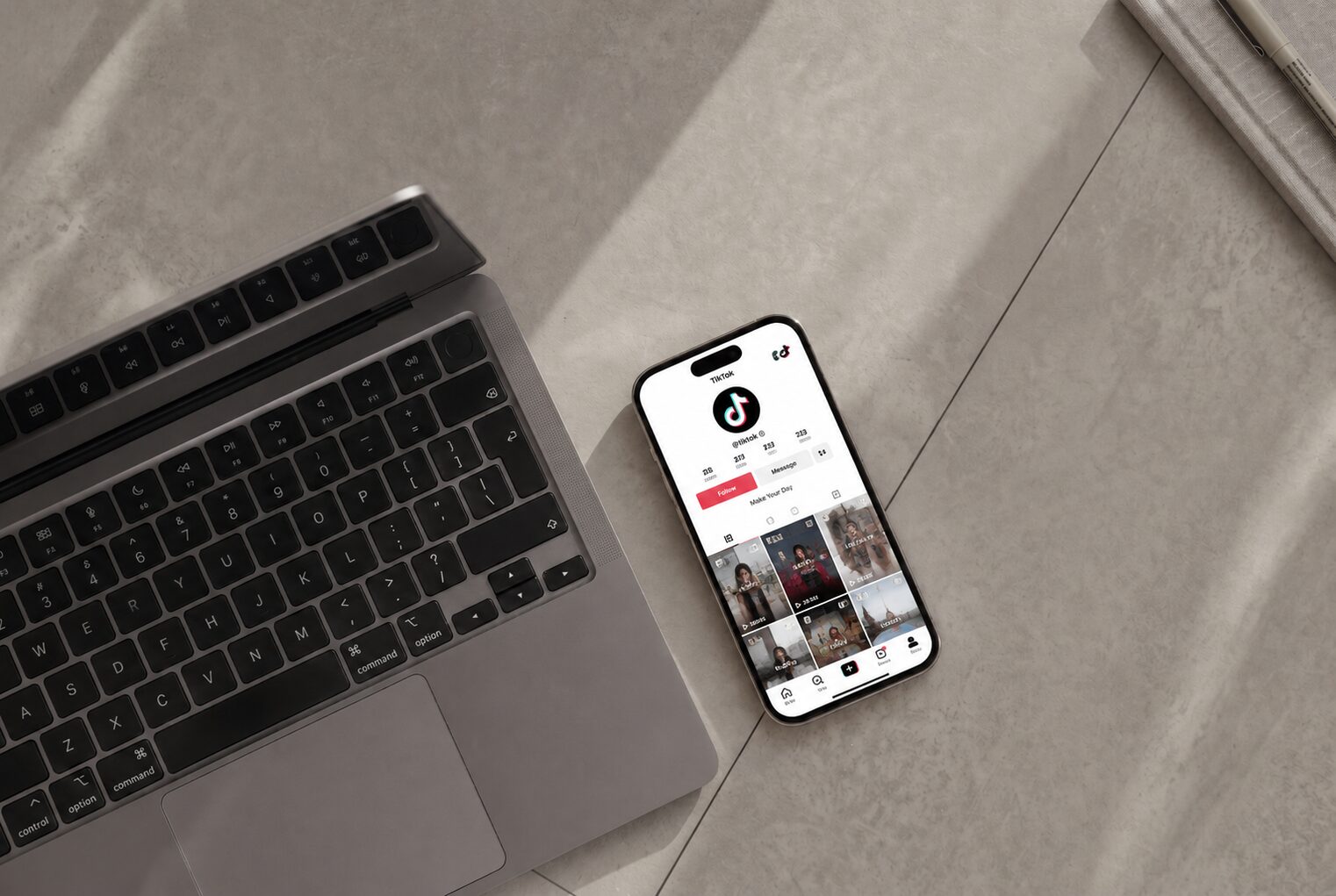 Phone showing a TikTok profile next to a laptop on a bright desk